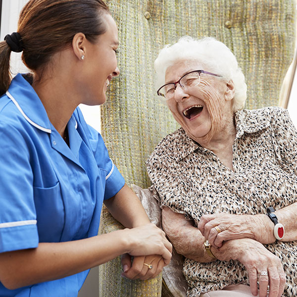 Senior woman sitting In chair and laughing with nurse In retirement home